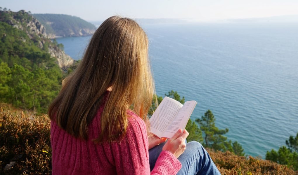 a woman reading a book on a cliff
