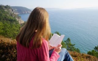 a woman reading a book on a cliff