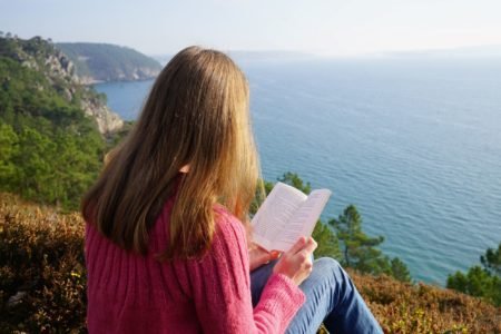a woman reading a book on a cliff