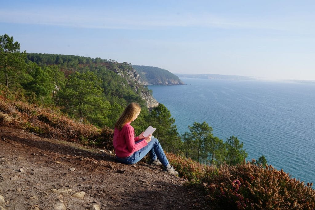 a woman reading a book on a cliff