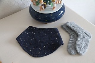 grey handknitted socks for a baby along with a blue bib with gold dots