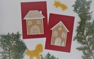 two red card with cardboard gingerbread houses on them next to some beeswax ornaments and branches