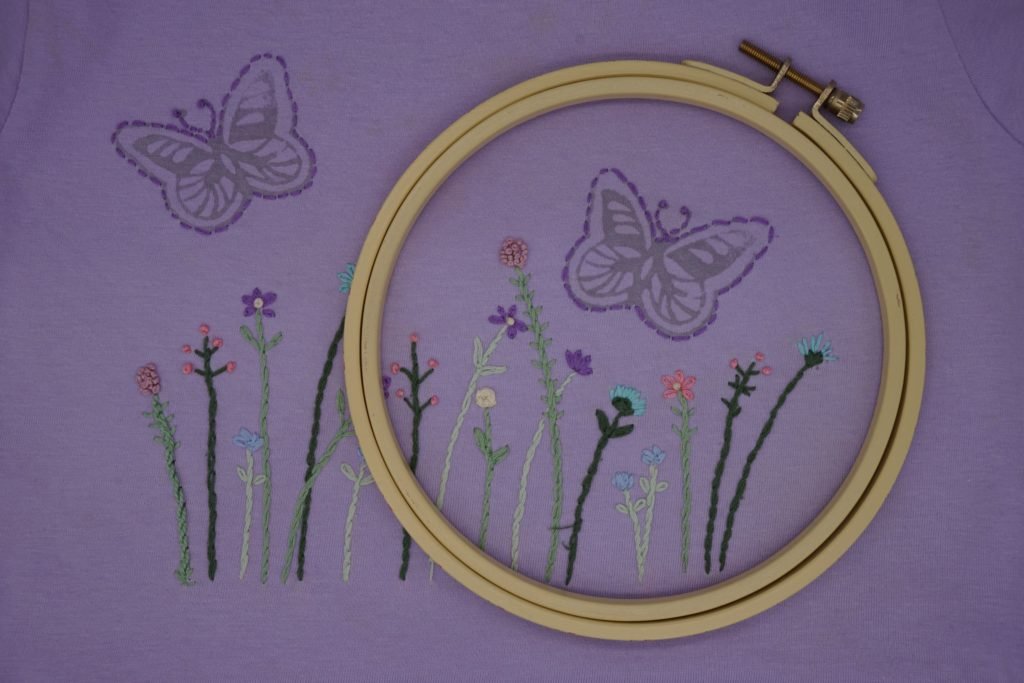 purple t shirt with some flower and butterly embroidery on it