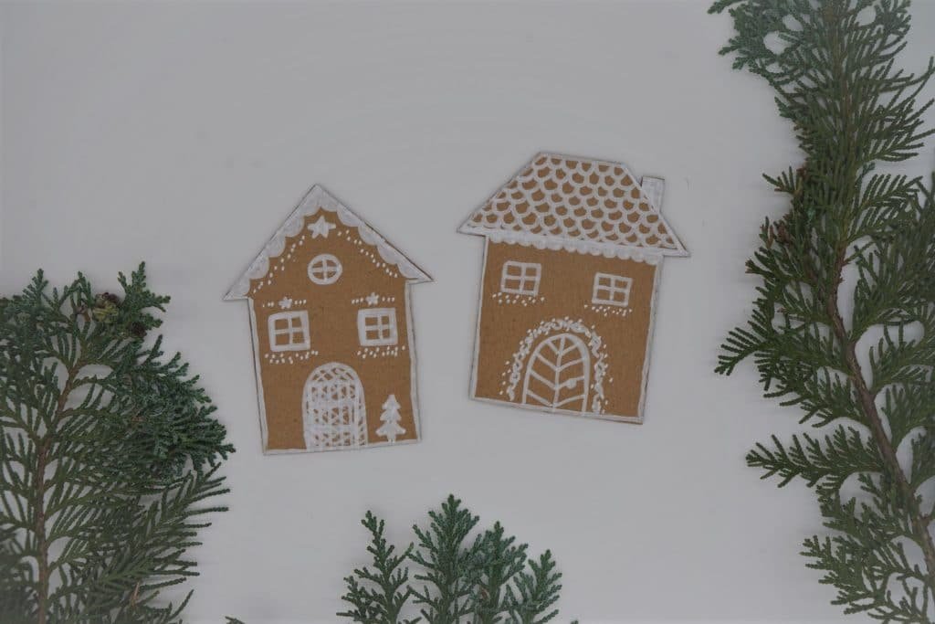 two gingerbread house made out of a cardboard box and some branches next to them