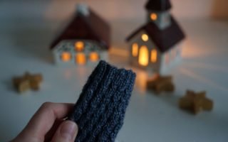 grey blue cabled baby sock in the making, some candle lit houses in the background