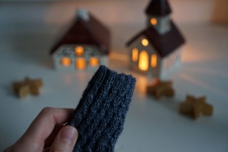 grey blue cabled baby sock in the making, some candle lit houses in the background