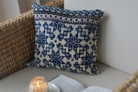 sweater pillow on an armchair next to a book and a burning candle