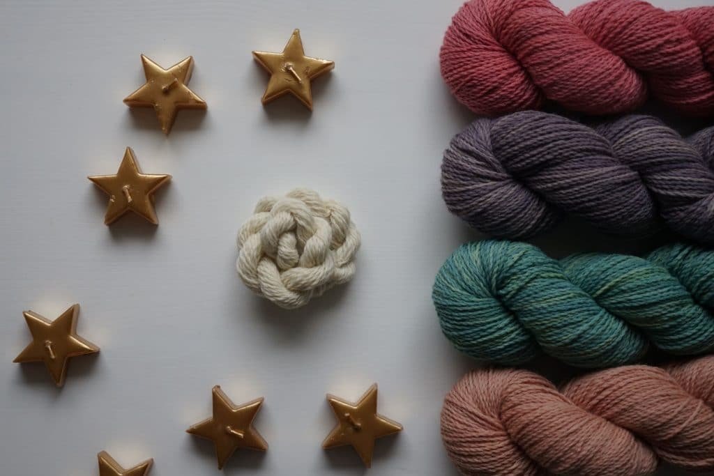 natural white mini skein in a circle next to some star shaped golden candles and four colourful skeins of yarn