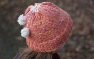 pink orange colorwork hat with two mini pompoms attached with strands of yarn