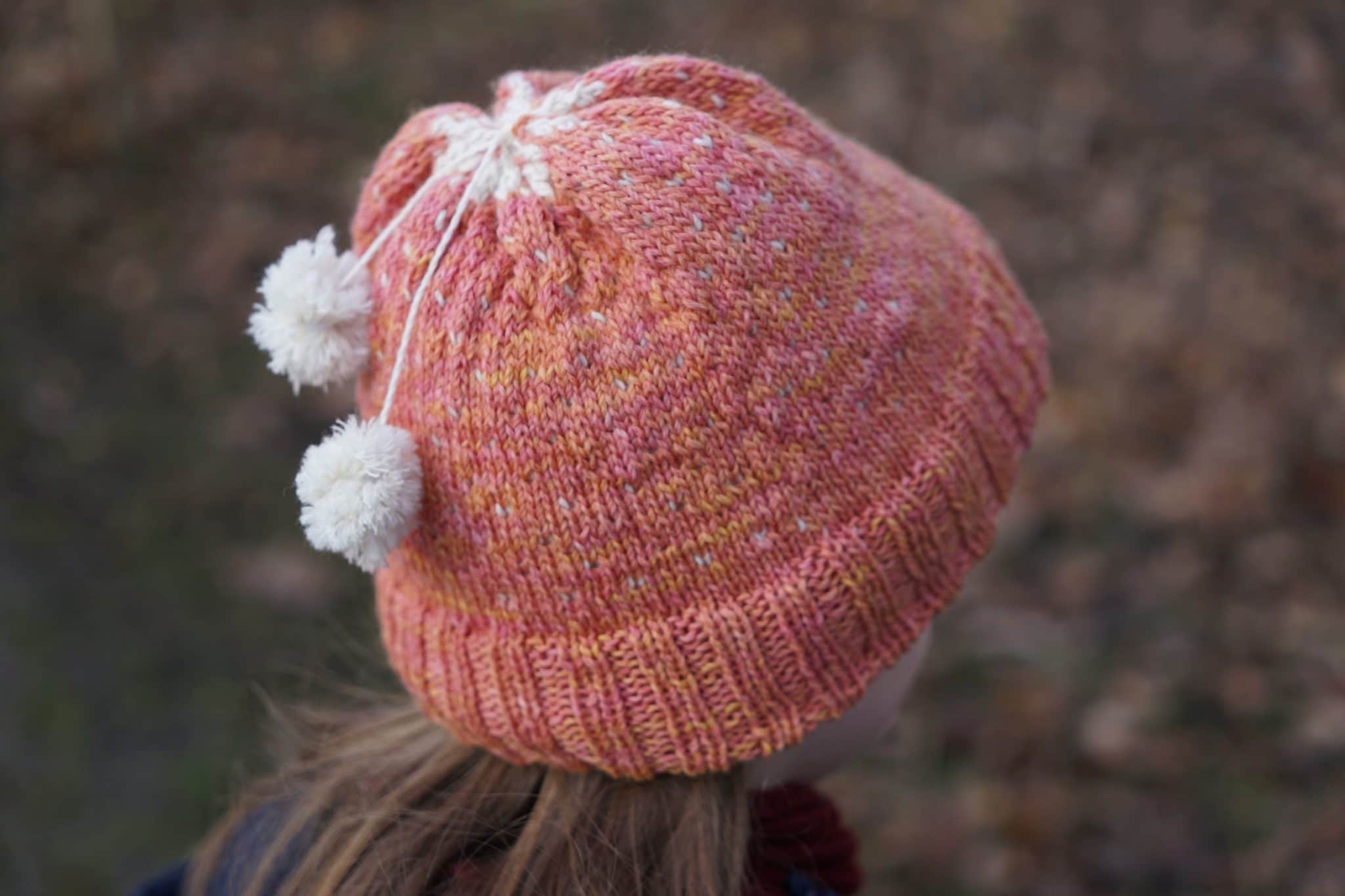 pink orange colorwork hat with two mini pompoms attached with strands of yarn