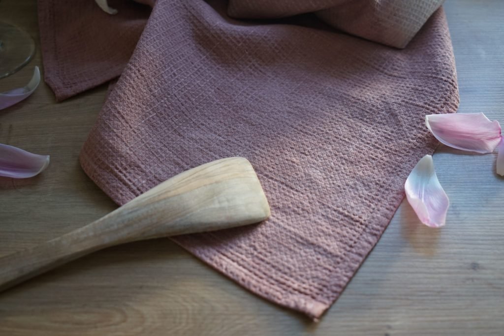 dusty pink kitchen towel, wooden spatula and some light pink tulip petals