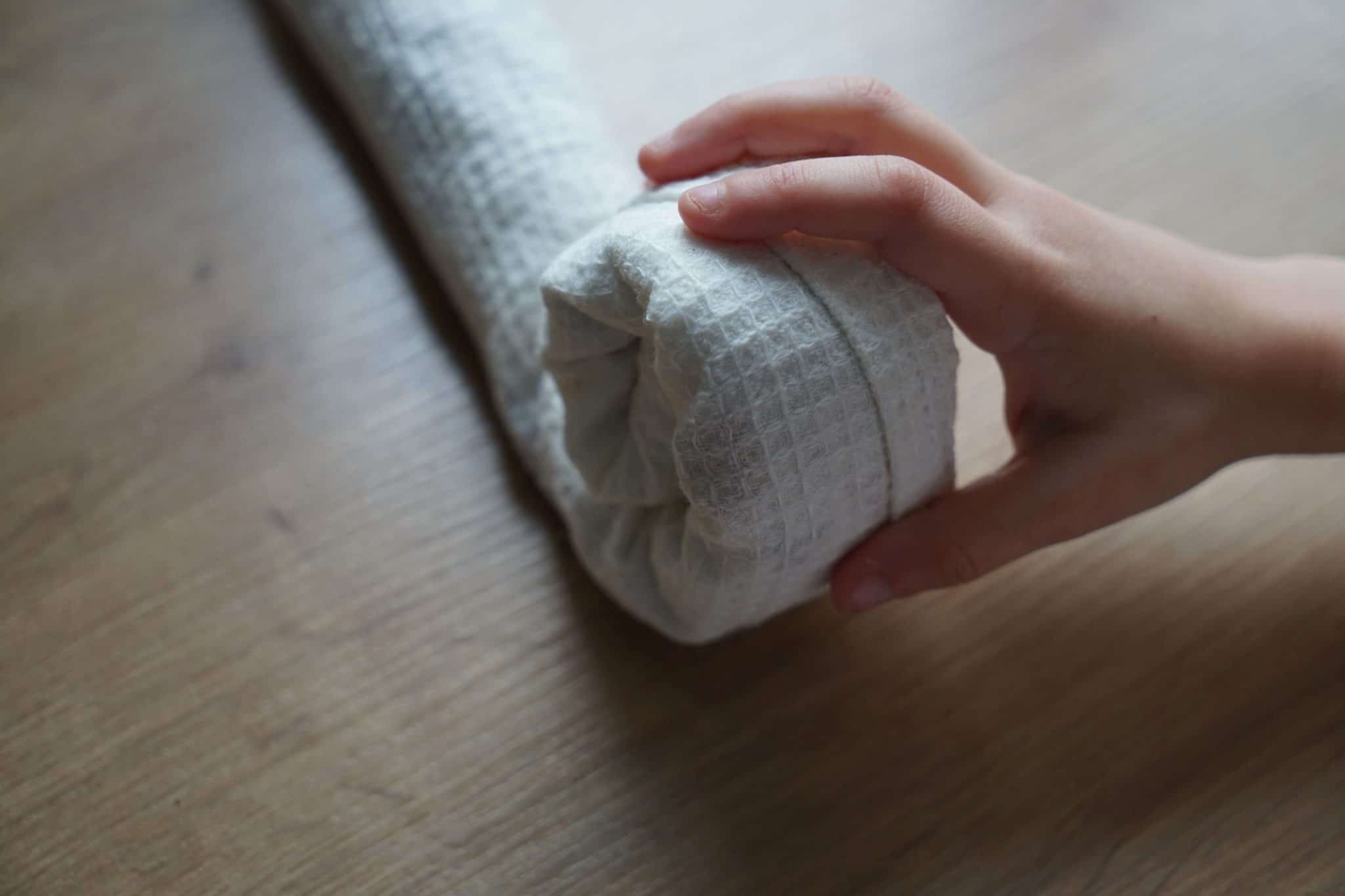 a hand rolling up a white kitchen towel to create a bundle