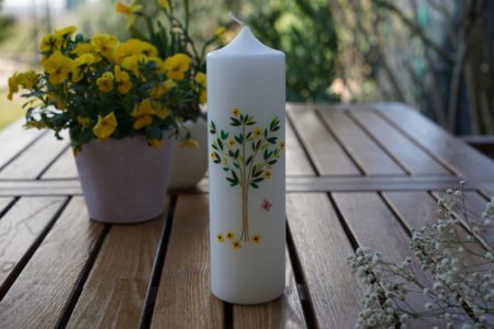 an embellished candle on a wooden table, some flowers in the fore- and background