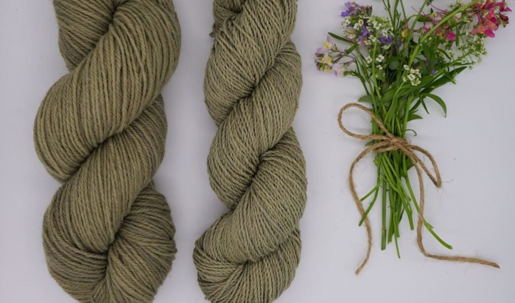 two skeins of dusty green yarn and a small bouquet of wildflowers next to them