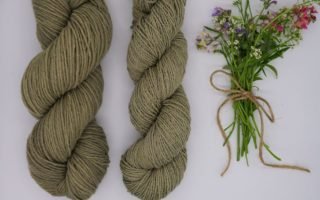 two skeins of dusty green yarn and a small bouquet of wildflowers next to them