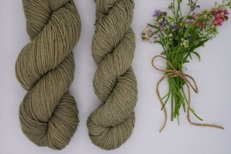 two skeins of dusty green yarn and a small bouquet of wildflowers next to them