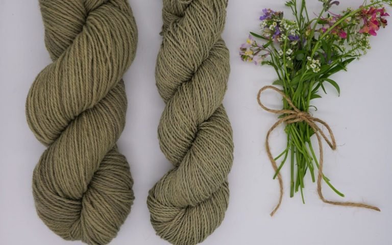 two skeins of dusty green yarn and a small bouquet of wildflowers next to them