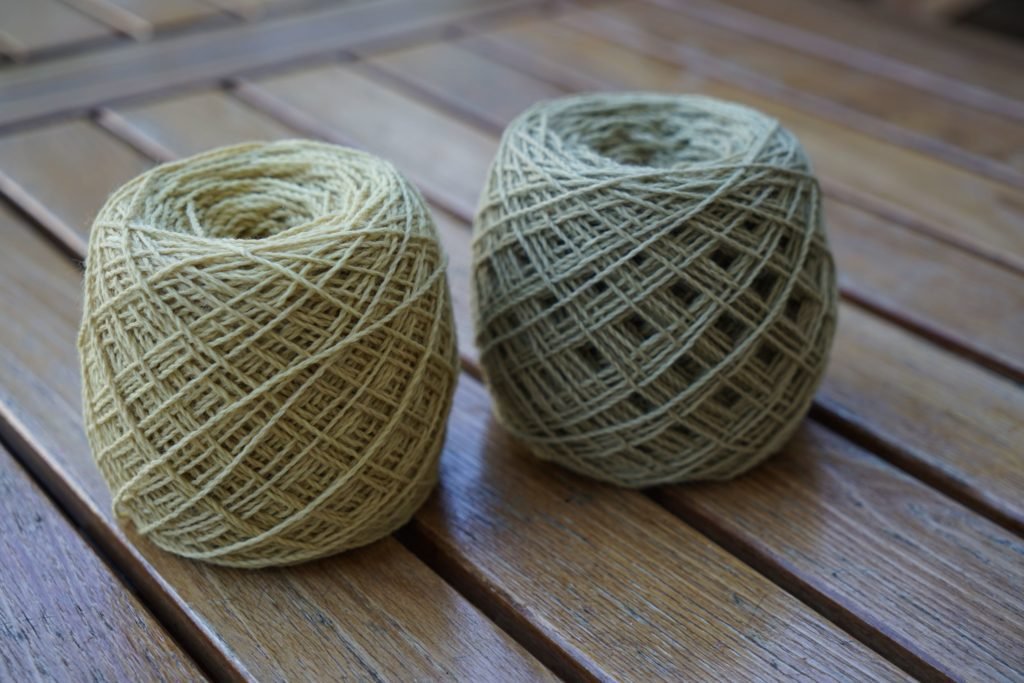 two cakes of yarn in light beige and dusty green on a wooden table