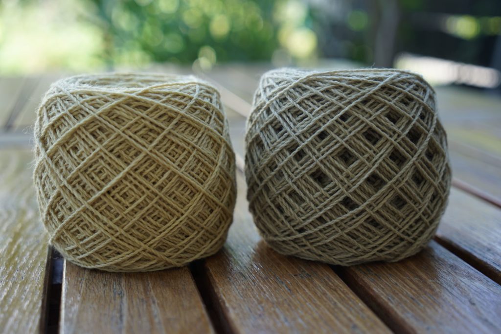 two cakes of yarn in light beige and dusty green on a wooden table