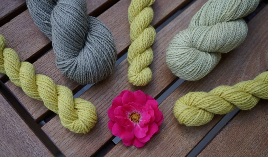 grey and yellow skeins of yarn and a pink rose in the middle