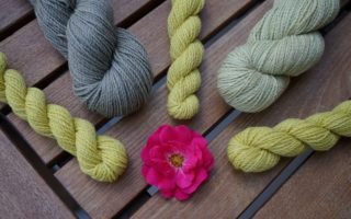 grey and yellow skeins of yarn and a pink rose in the middle