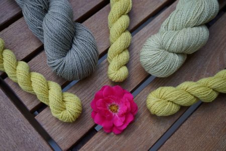 grey and yellow skeins of yarn and a pink rose in the middle