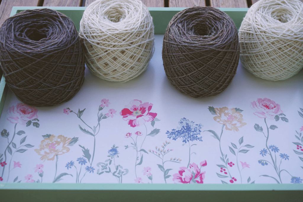 two white and two grey cakes of yarn on a tablet painted with flowers and a mint border
