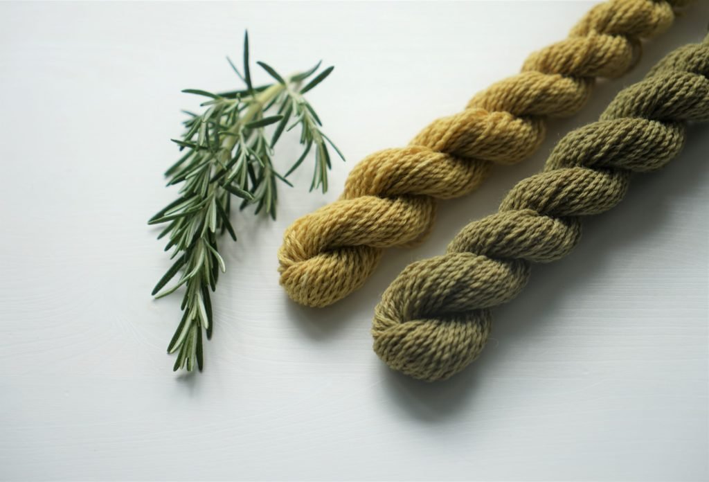 two yellow and green mini skeins of yarn and a rosemary branch next to it