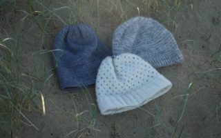 three knitted hats in blue, greys and white laying on a sand dune