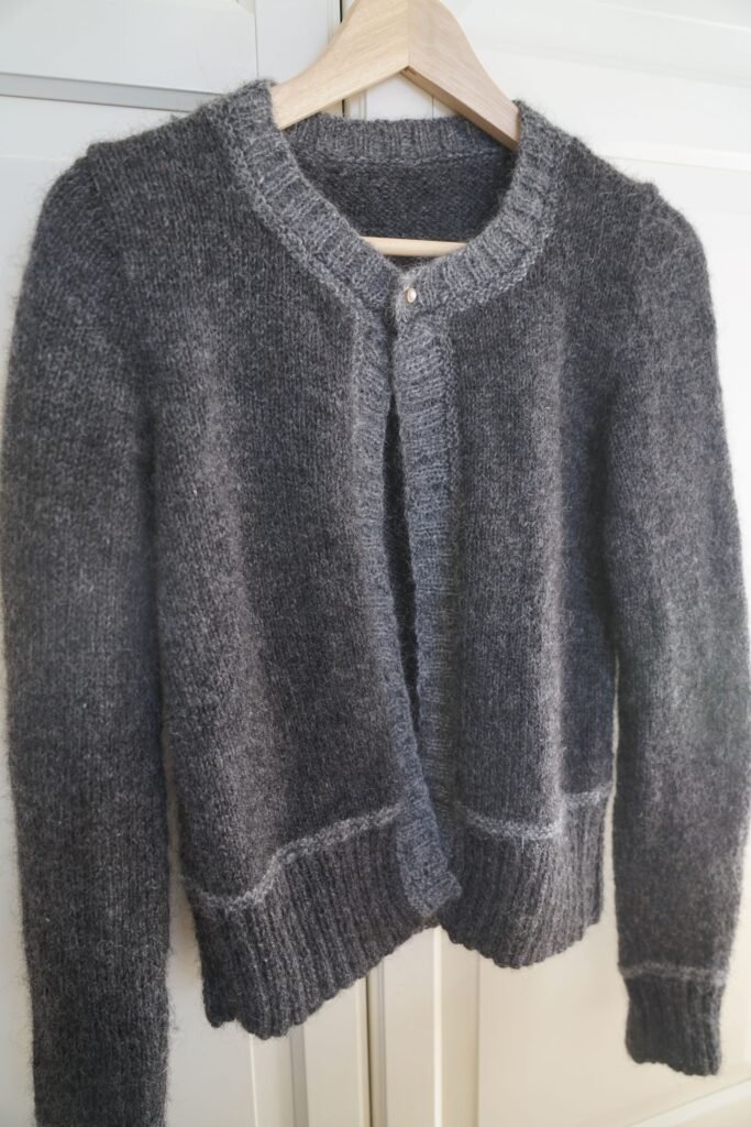 handknitted dark and light grey cardigan on a hanger, hanging on a white armoire