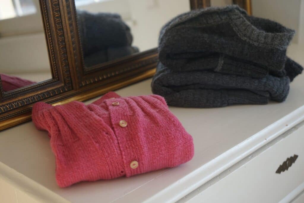 three cardigans on a white dresser with a mirror behind them