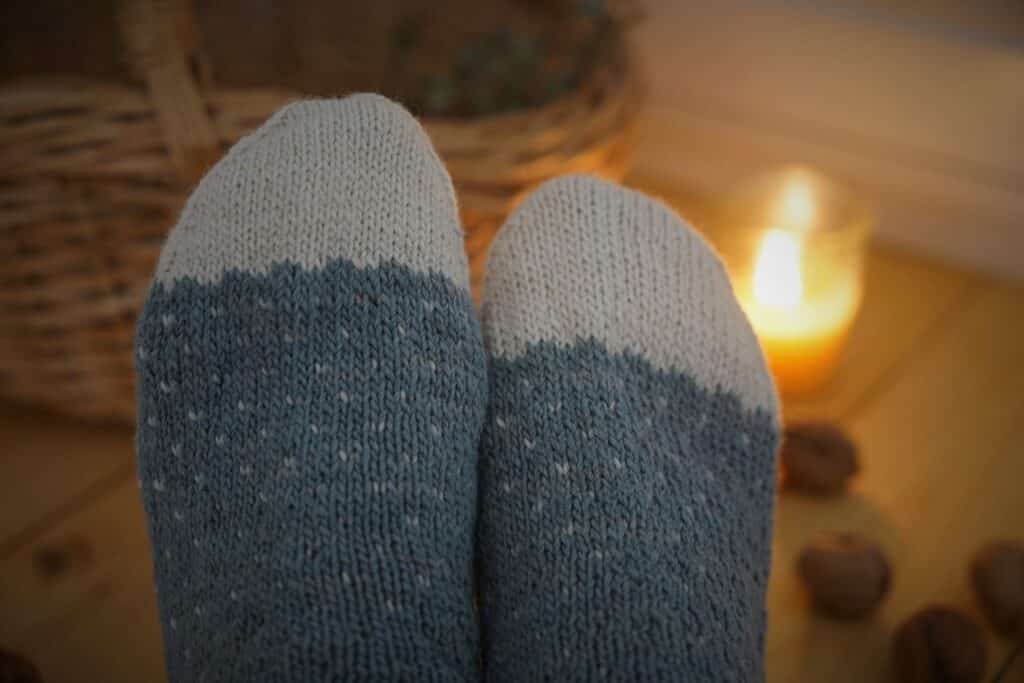 tips of two socks in front of a beeswax candle, a basket and a wooden floor