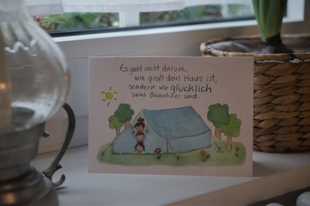 greeting card with german writing on a windowsill, next to a candle holder and some plants