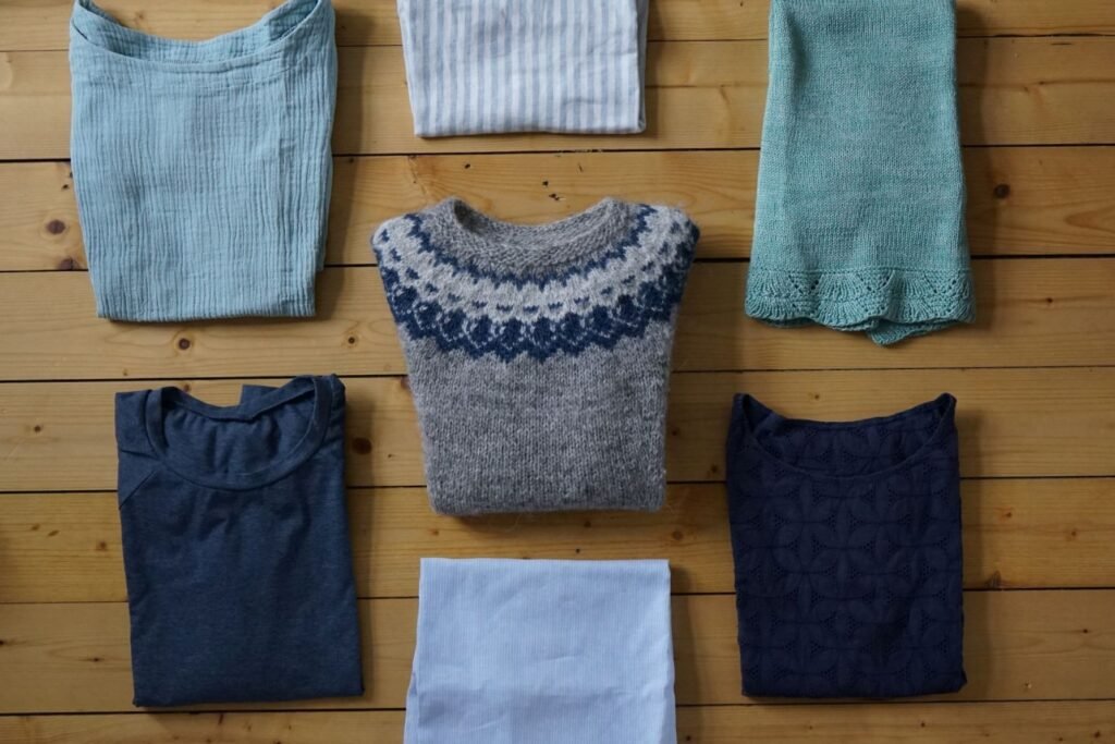 handmade garments in blues, greys and greens laying on a wooden floor