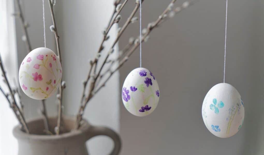 three hand painted eggs with floral motifs hanging from a few willow branches