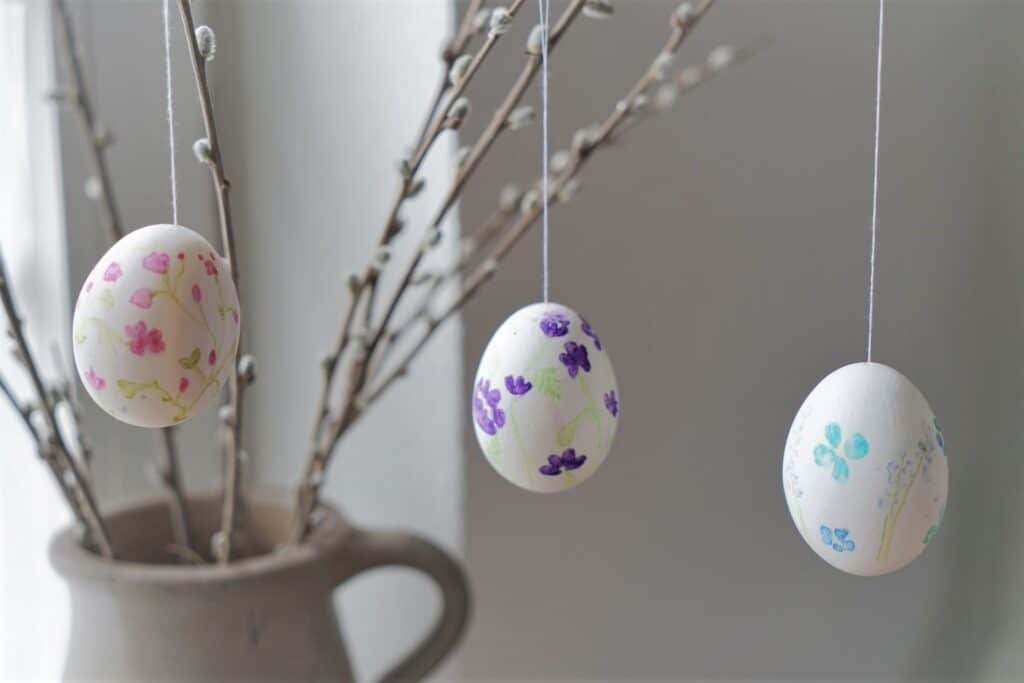 three hand painted eggs with floral motifs hanging from a few willow branches