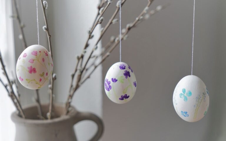 three hand painted eggs with floral motifs hanging from a few willow branches