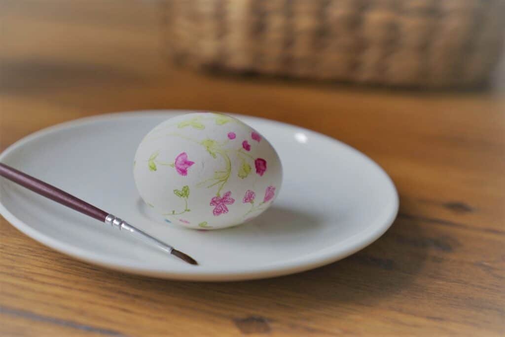 an egg in the process of being painted on a small white plate together with a paintbrush