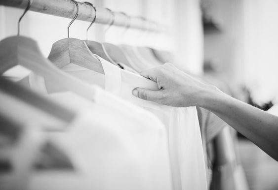 black and white picture of a rack of clothing and a hand touching one of the shirts