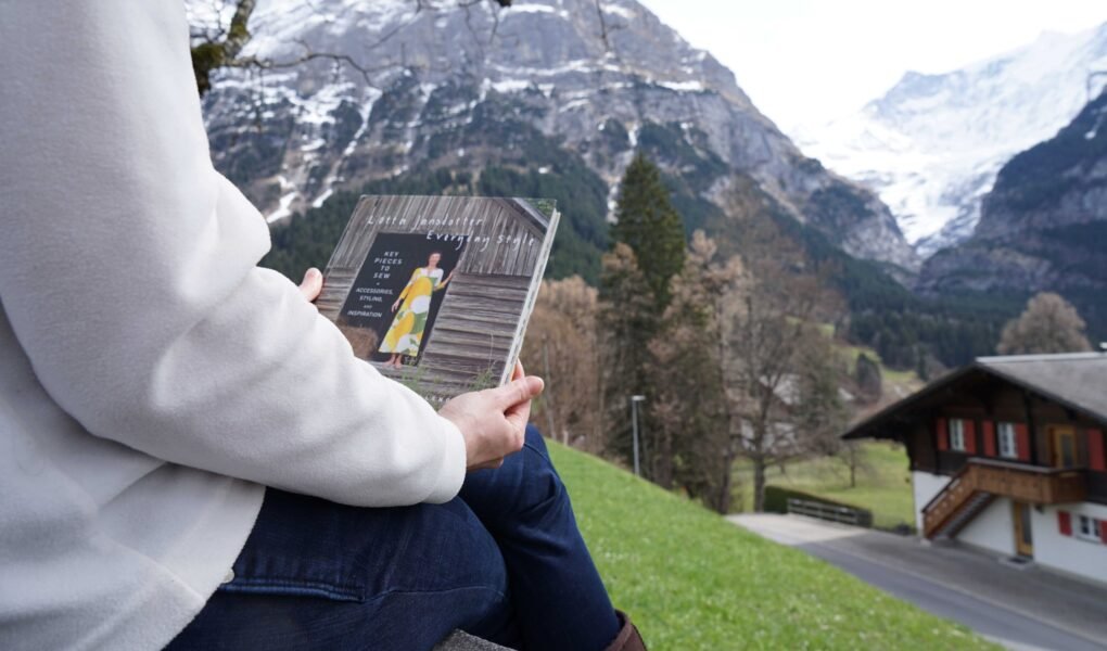 a woman sitting in an alpine scenery holding the book everyday style by lotta jansdotter
