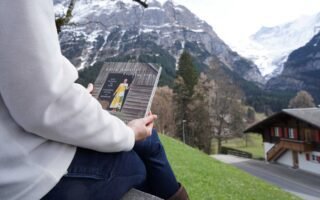 a woman sitting in an alpine scenery holding the book everyday style by lotta jansdotter