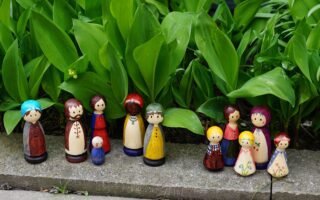 eleven colorful hand painted wooden peg dolls in a garden setting