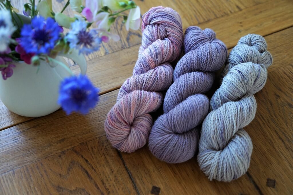 three variegated skeins of yarn in purple, blue and pink on a wooden table