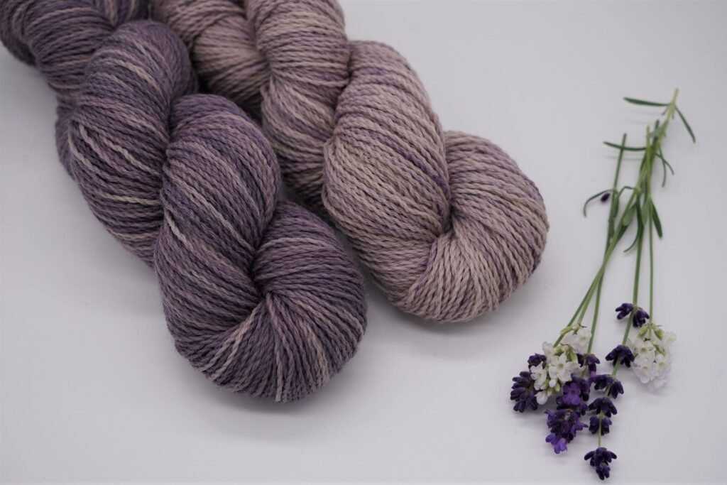 two purple skeins of yarn in different shades and some lavender on a white surface