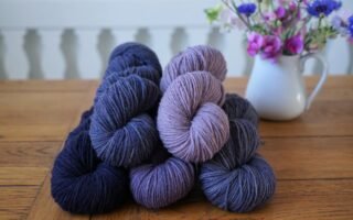 stack of purple and blue skeins on a wooden table and a milk jug filled with flowers