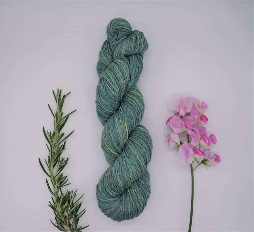 blue, green and yellow skein of yarn next to some sweet pea blooms and a rosemary branch