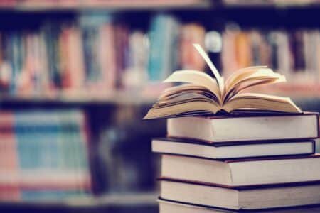 a stack of books in front of a bookshelf, the book at the top is open