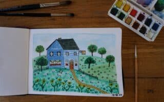 open sketchbook with watercolor and ink painting of a blue yarn shop in the hills