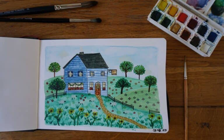 open sketchbook with watercolor and ink painting of a blue yarn shop in the hills