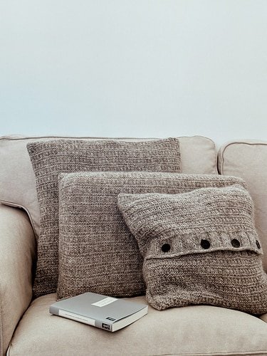 three handknitted beige-brown pillows sitting on a beige couch next to a journal